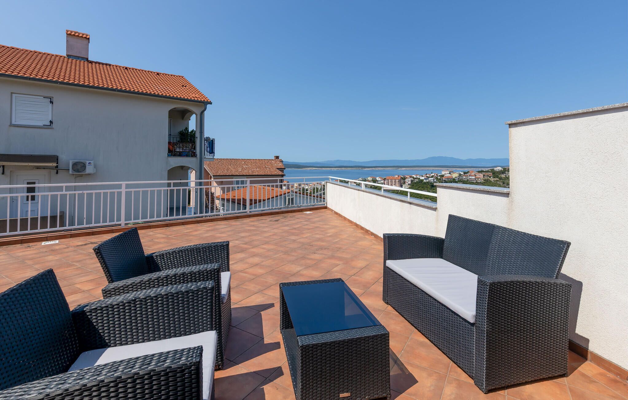 A rooftop terrace with wicker furniture and a view of the sea.