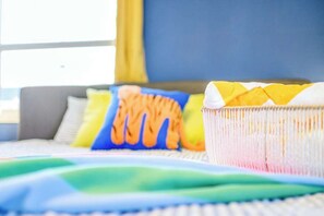 A bed with colorful bedding and pillows, a striped blanket, and a window with curtains.