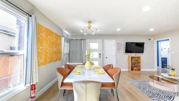 Un coin repas avec une table dressée pour quatre personnes, entourée de chaises, d’un téléviseur et d’une bibliothèque.