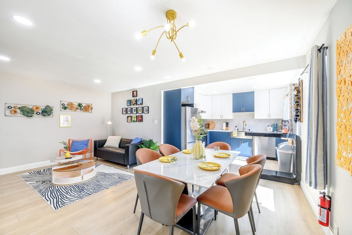 A modern living room with a dining area, kitchen, and a staircase leading to an upper floor.