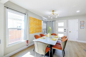 A dining area with a white table, orange chairs, a yellow vase, and a patterned wall. - Cheerful Modern 4 Beds | Bright & Easy  to BART (San Leandro)