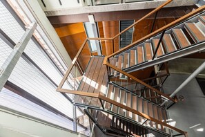 Eine mehrgeschossige Innenarchitektur-Treppe mit Metallgeländern und Holzstufen, umgeben von Glaswänden und Stahlträgern.