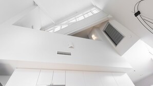 Un intérieur moderne avec des murs blancs, un plafond en pente et une bouche d’aération visible.