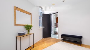 Un couloir moderne avec un plancher en bois, un mur blanc, une porte noire, un banc et une petite table sur laquelle est posée une plante.