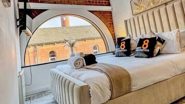 A bedroom with a bed, a skylight, a brick wall, and a view of a building.
