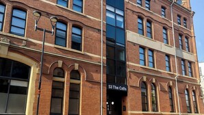 A multi-story brick building with large windows and a sign reading "53 The Calls".
