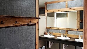 A bathroom with a rustic design, featuring a large mirror, two sinks, and wooden shelves.
