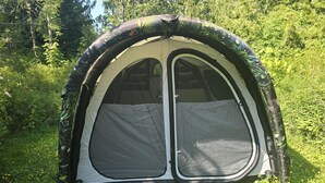 A dome-shaped tent with a mesh window and a rainfly, set in a forested area.