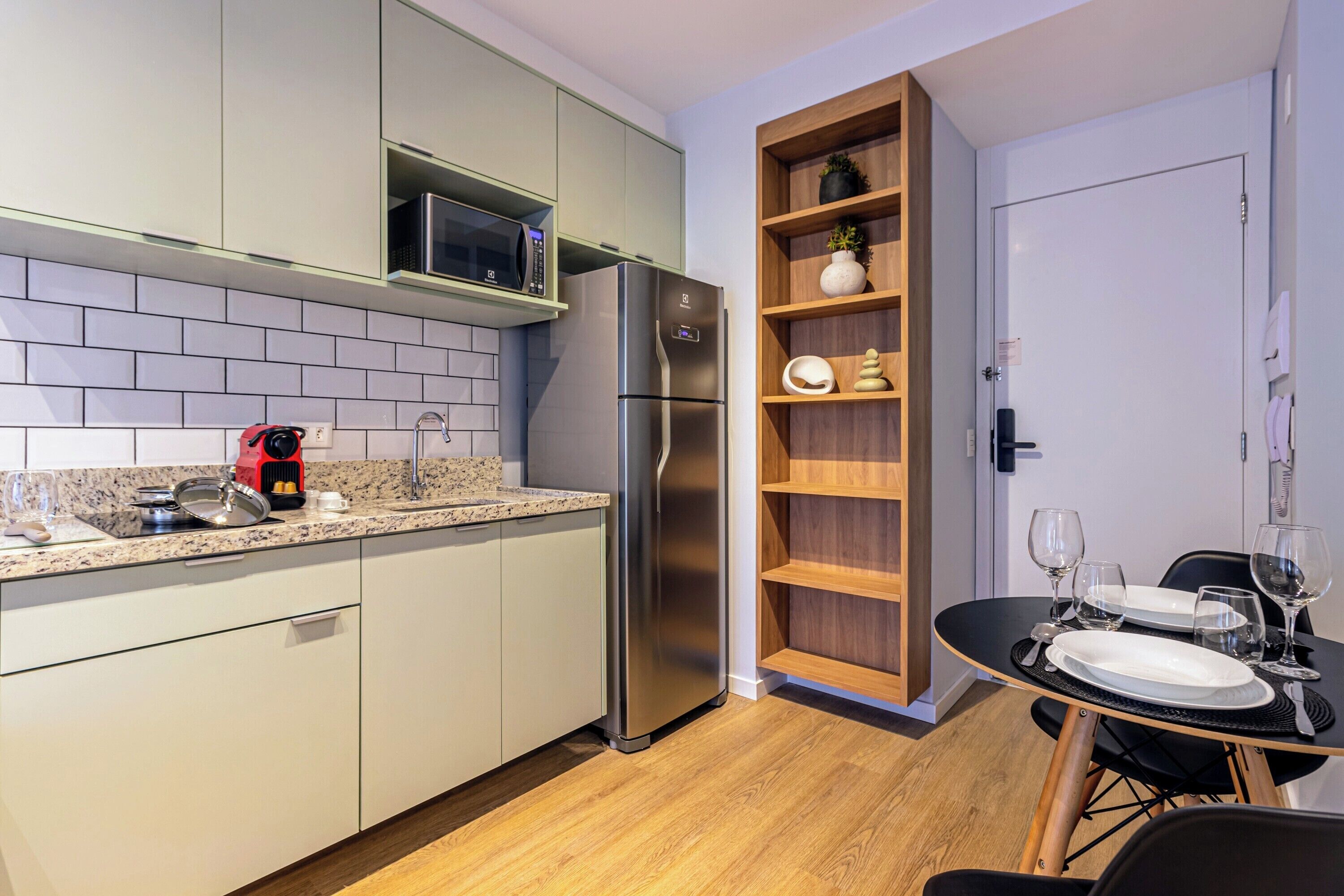A modern kitchen with a stainless steel refrigerator, a microwave, and a coffee maker on the countertop. There is a dining table with plates and glasses set up.