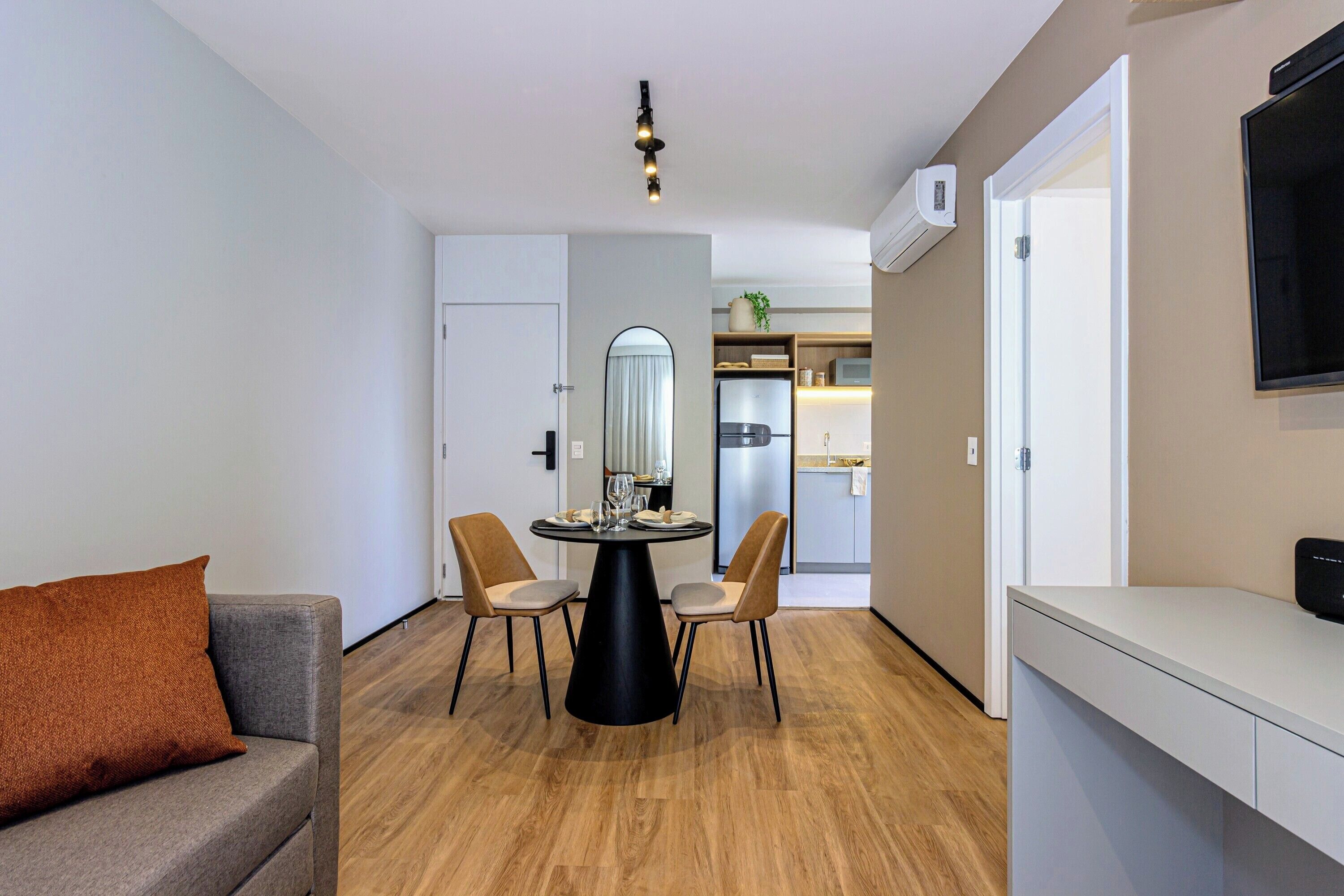 Un espacio habitable compacto con mesa de comedor, dos sillas, un sofá, televisor y una zona de cocina al fondo.