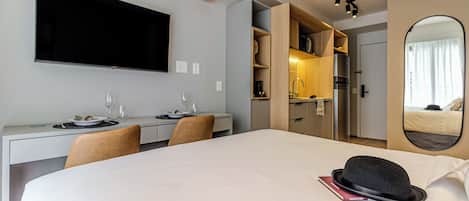 Een hotelkamer met een bed, een bureau, een flatscreen televisie, een spiegel en een kitchenette.