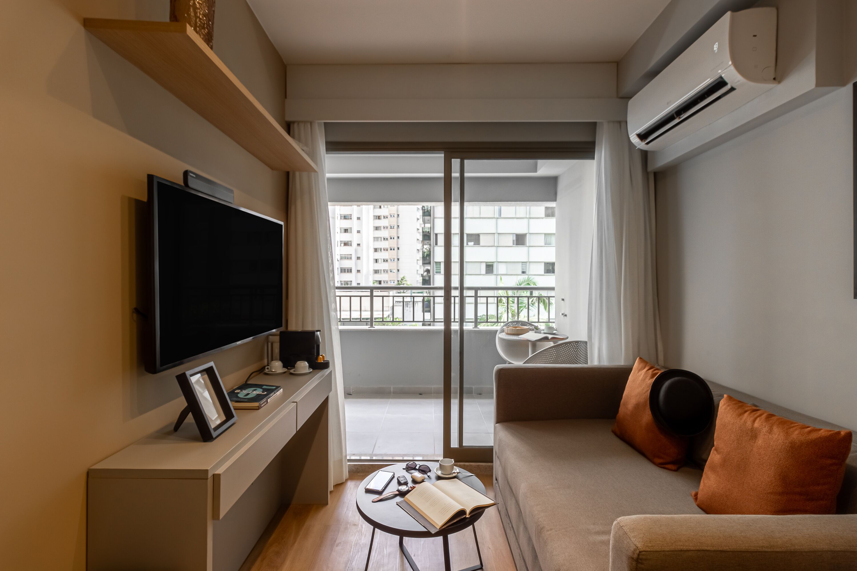 Una sala de estar moderna con un televisor de pantalla plana, un sofá, una mesa de centro y un balcón con vistas a edificios.
