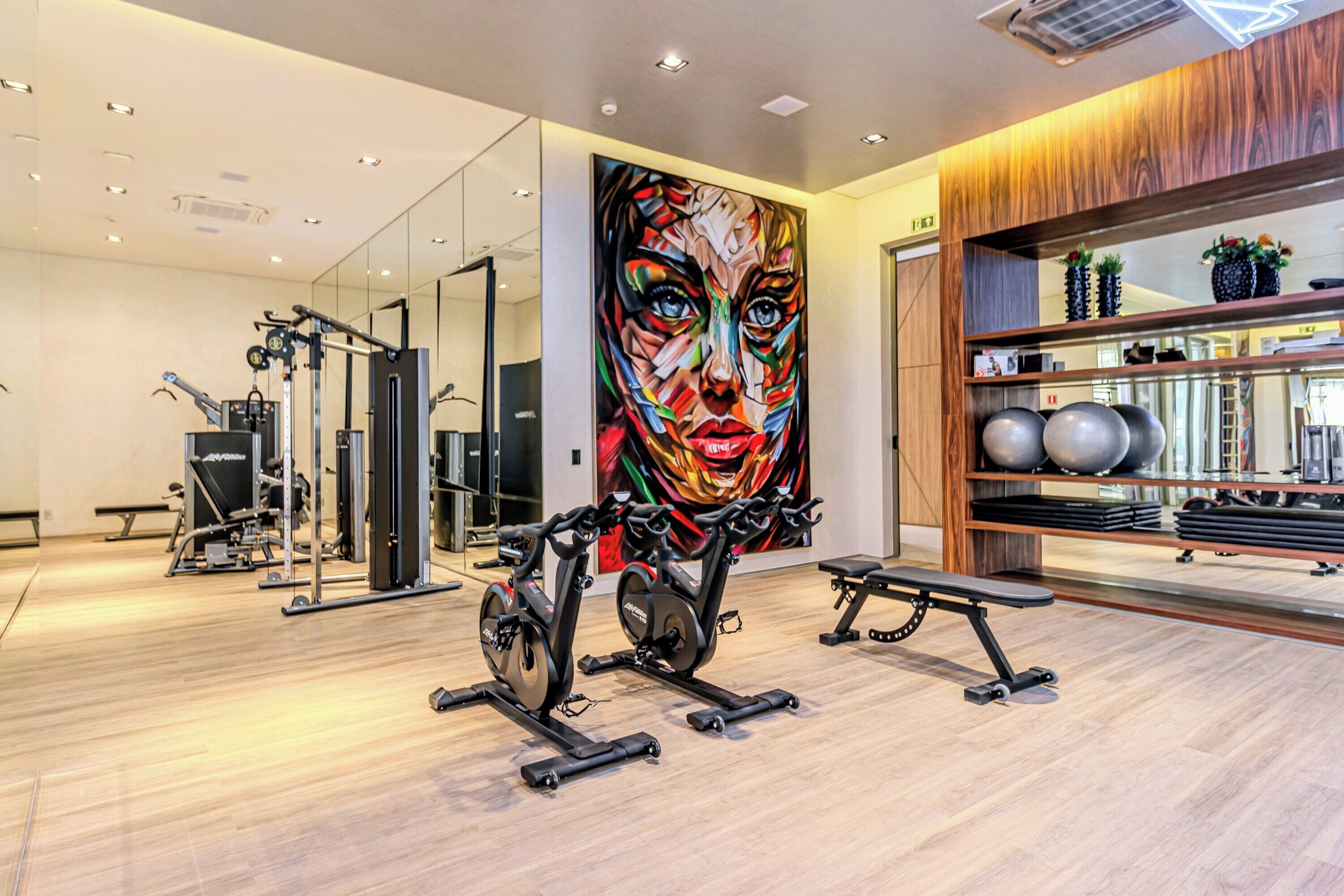 A modern gym with exercise equipment, a large mirror, and a colorful abstract painting on the wall.