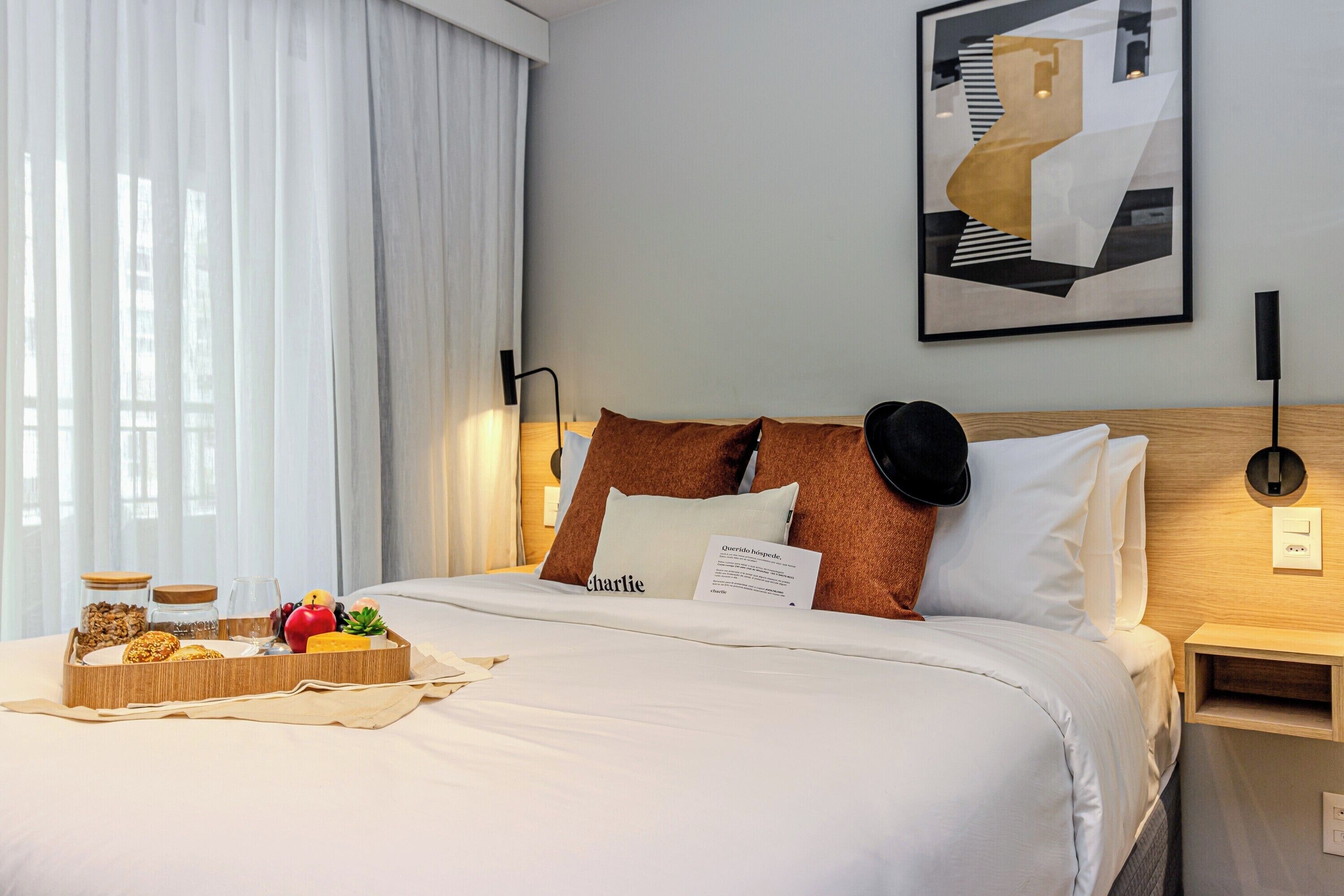 Een hotelkamer met een net opgemaakt bed, een nachtkastje met een lamp, een dienblad met ontbijtartikelen en een schilderij aan de muur.