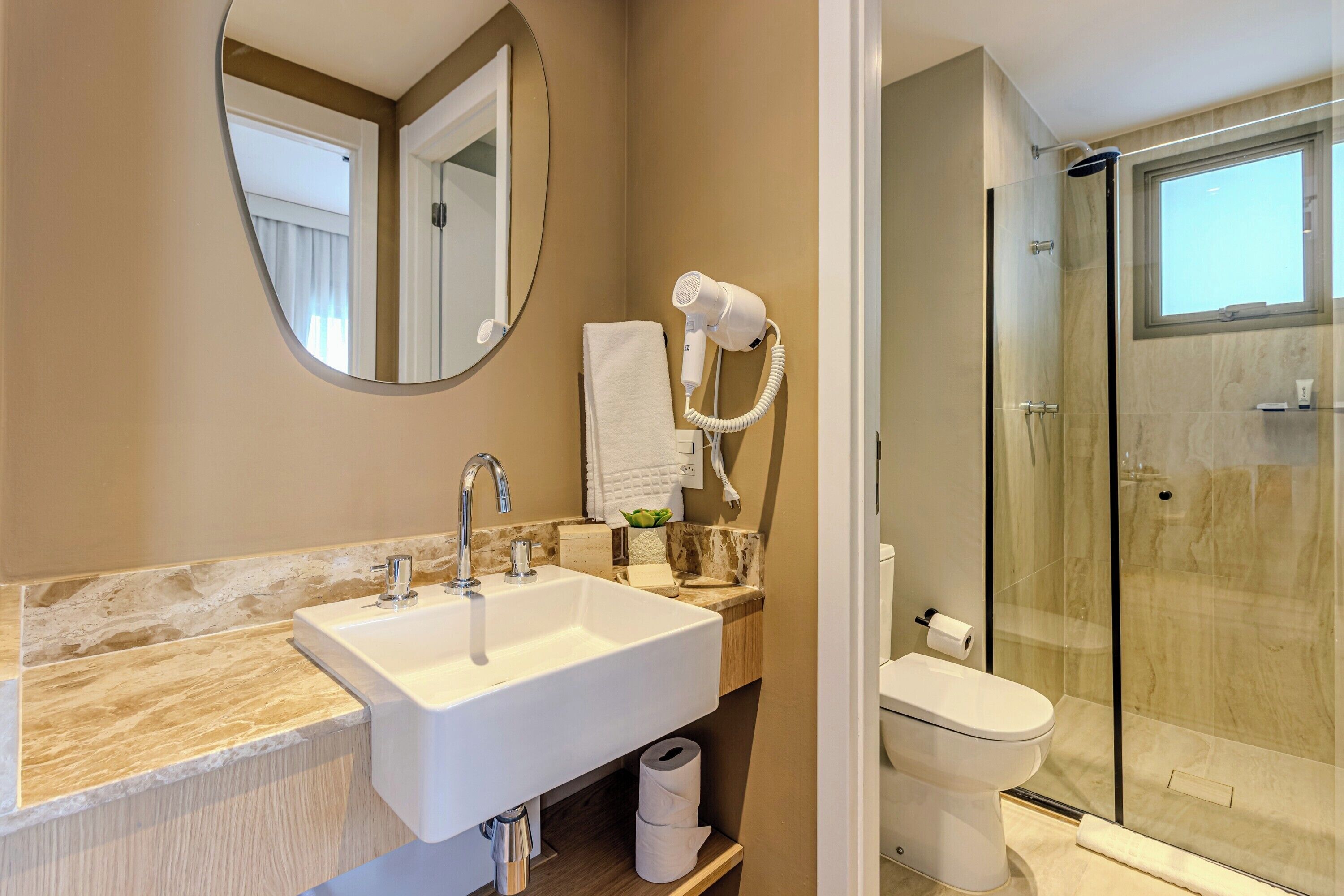 A bathroom with a large sink, a mirror, a towel rack, a hairdryer, and a glass-enclosed shower.