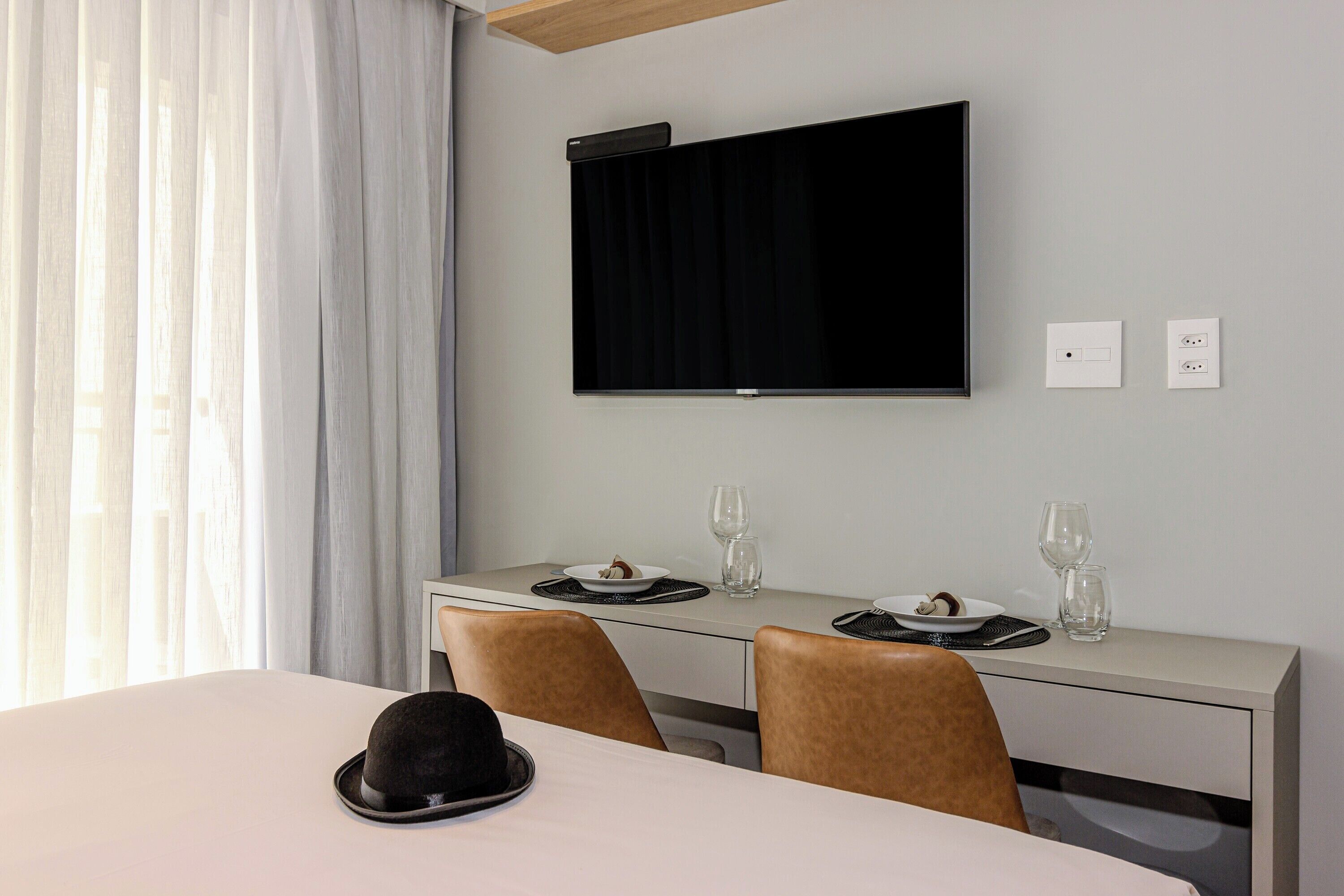 Habitación de hotel con zona de comedor que incluye una mesa, sillas, un televisor montado en la pared y dos tomas de corriente.