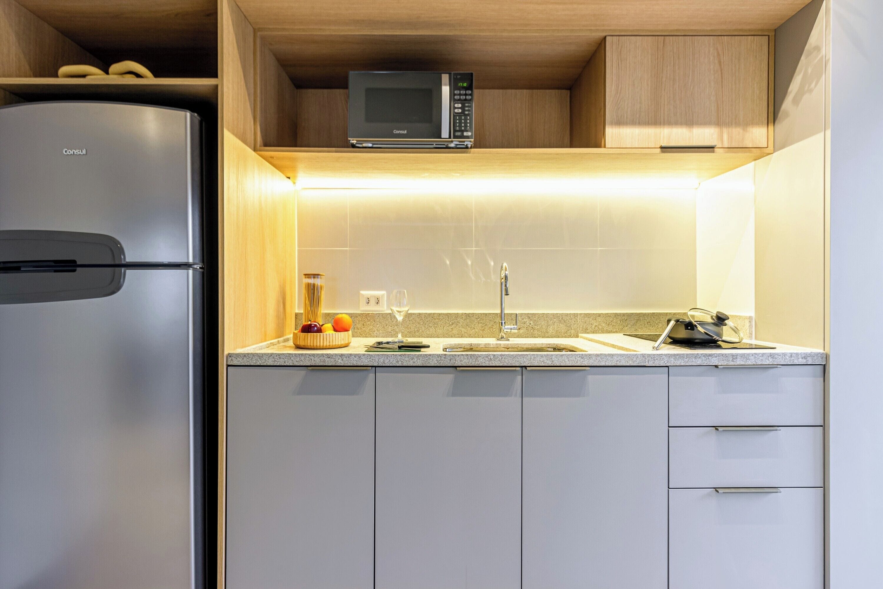 A kitchen with a refrigerator, microwave, sink, and cabinets.