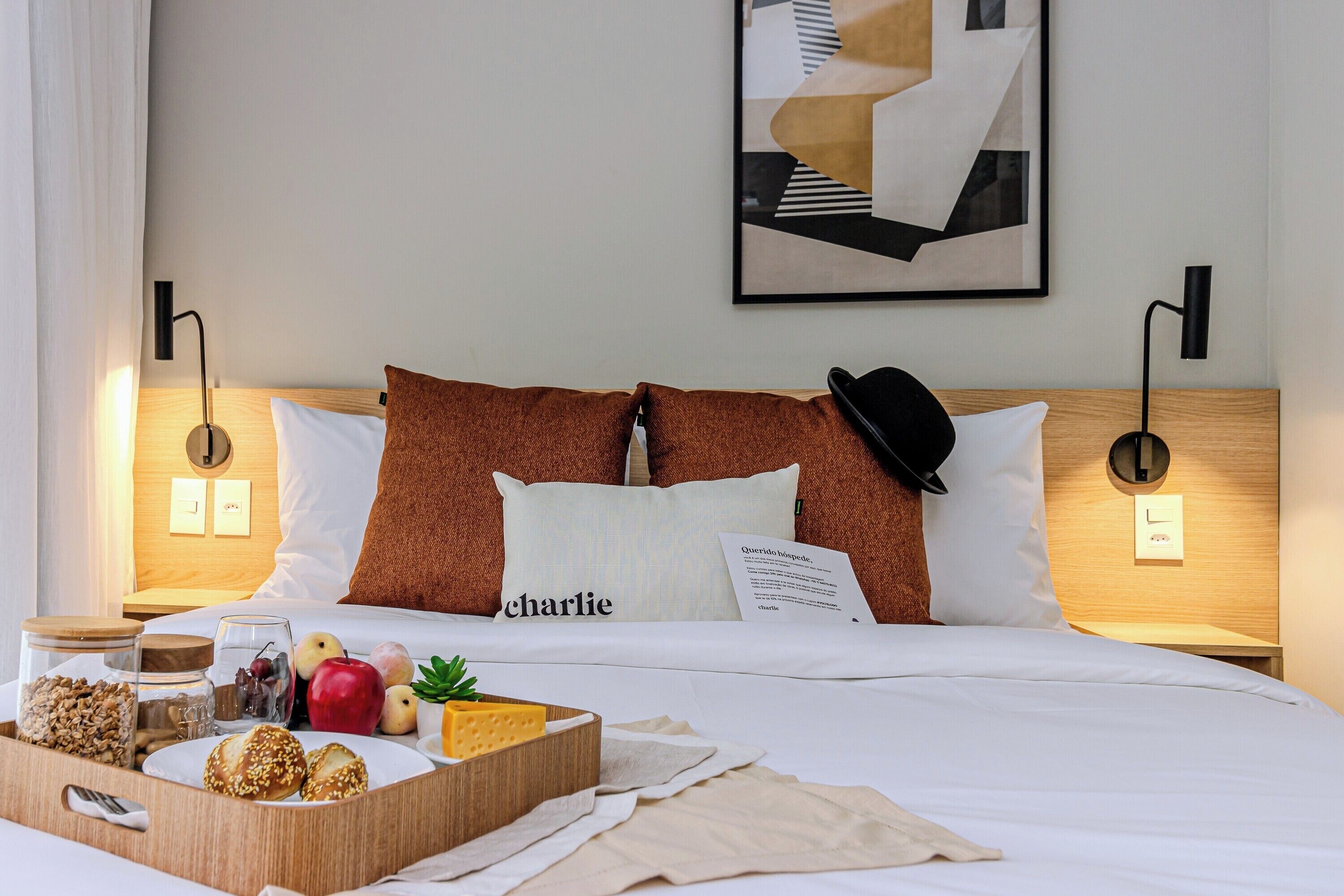 A neatly made bed with a tray of breakfast items, a framed picture on the wall, and a bedside lamp.
