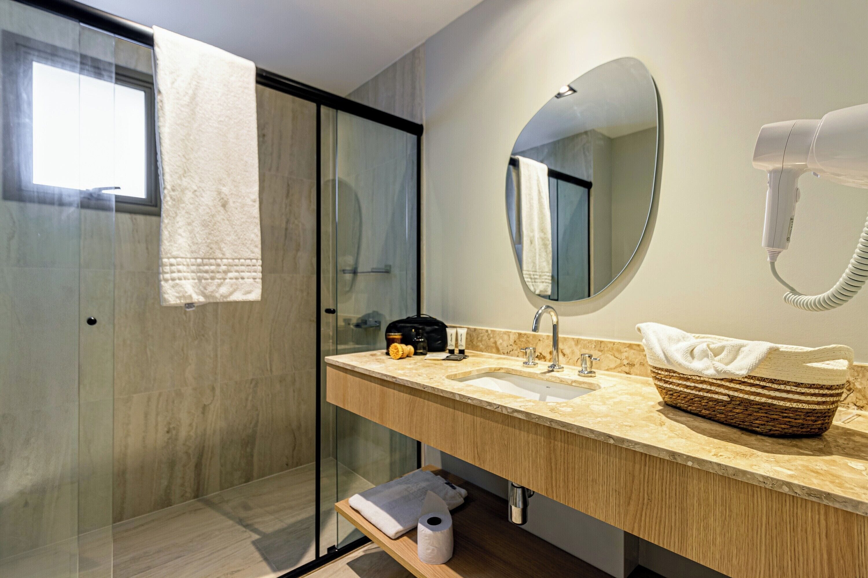 A modern bathroom with a glass shower enclosure, a wooden vanity, a large mirror, and a hairdryer mounted on the wall.