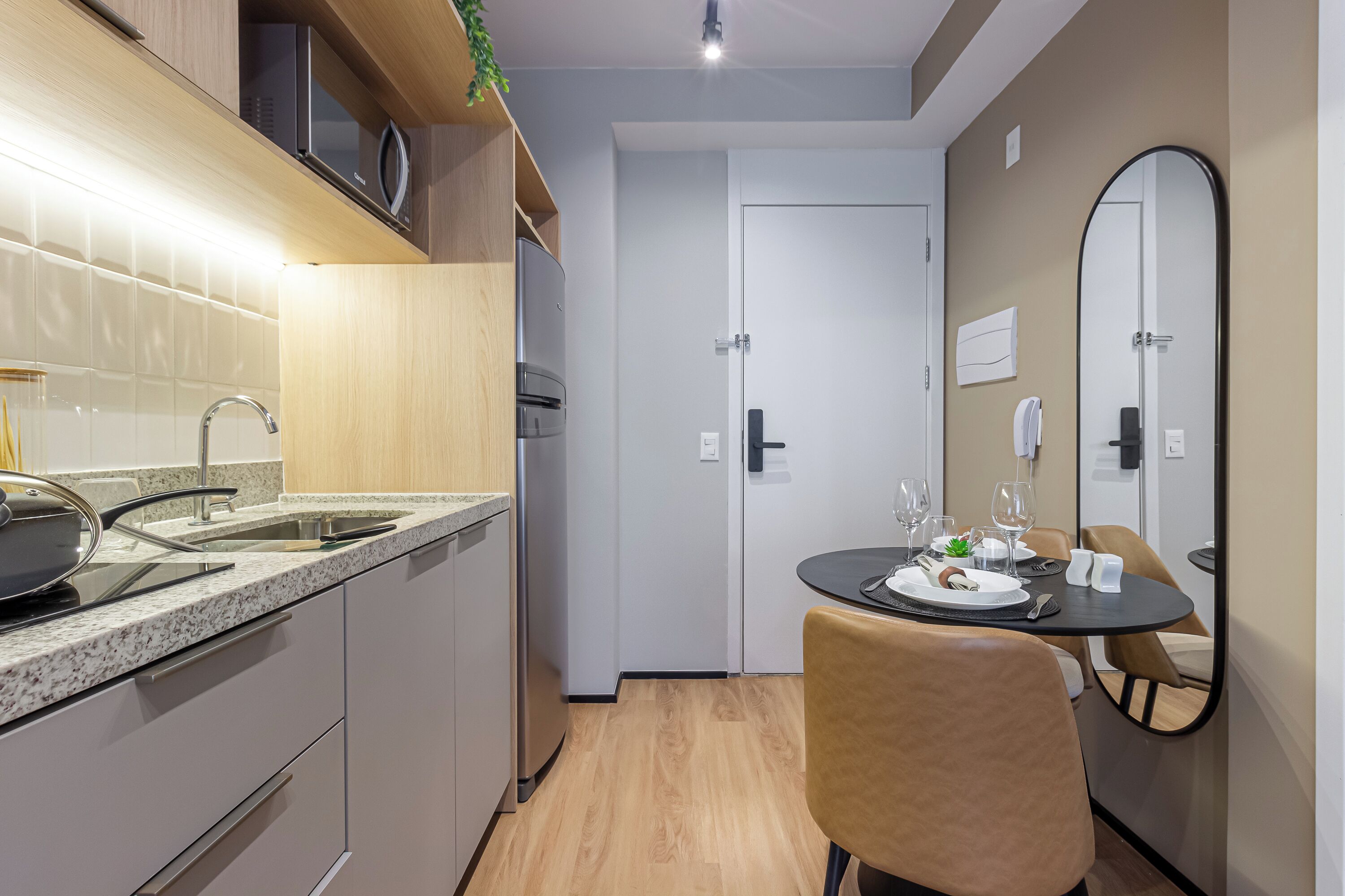 Cocina compacta con microondas, pileta y electrodomésticos modernos. Hay un comedor con una mesa dispuesta para dos, una silla y un espejo en la pared.