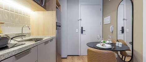 Cocina compacta con microondas, pileta y electrodomésticos modernos. Hay un comedor con una mesa dispuesta para dos, una silla y un espejo en la pared.