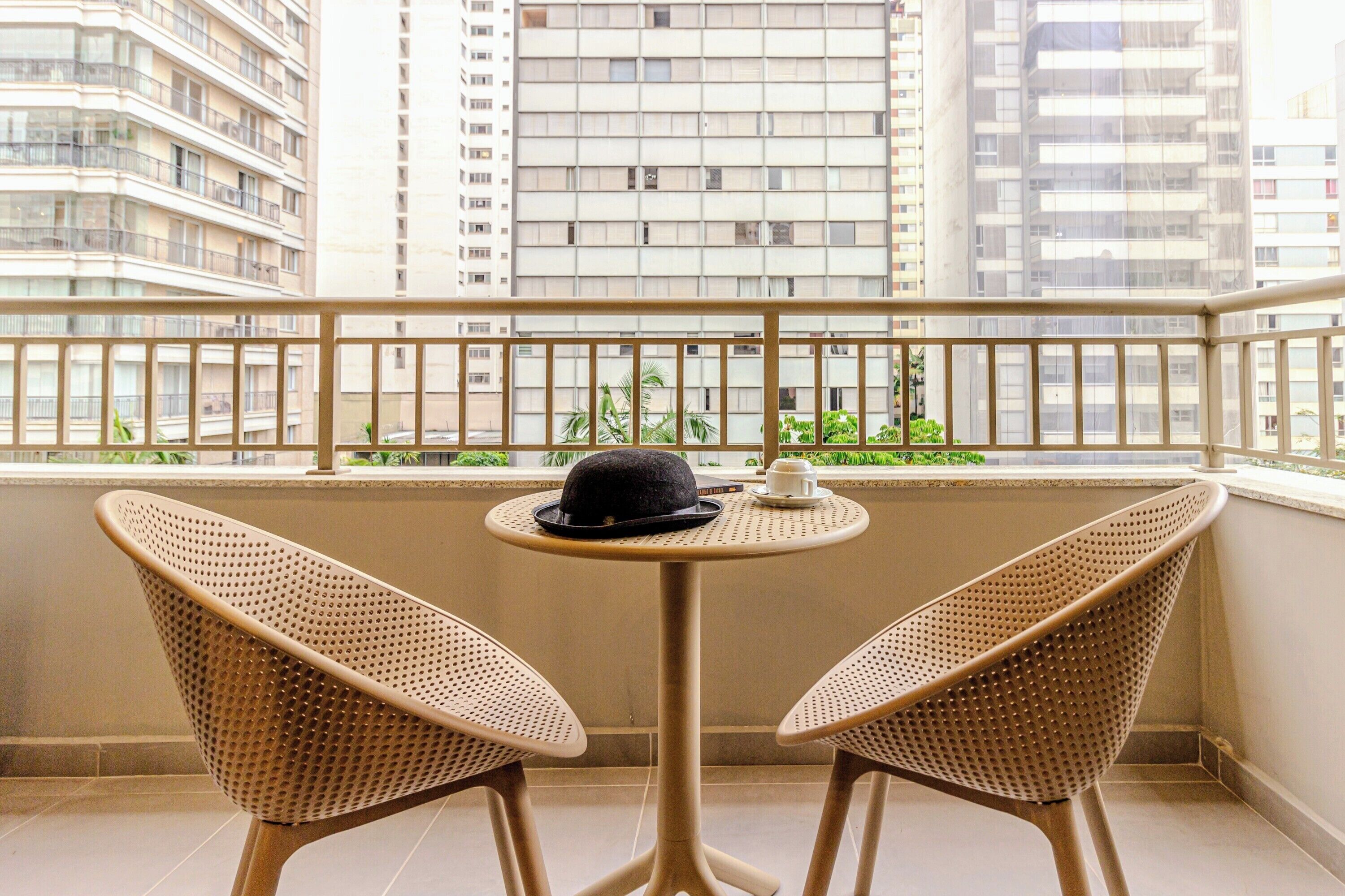 Un balcón con dos sillas de mimbre y una mesita, con vistas a un paisaje urbano de edificios altos.