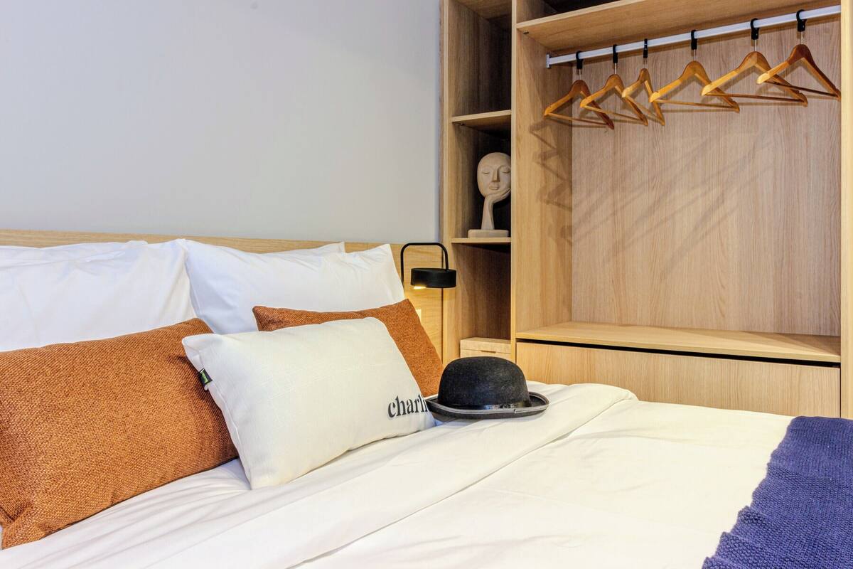 A neatly made bed with white and brown bedding, a black hat, and a pillow with the name "Charlie".