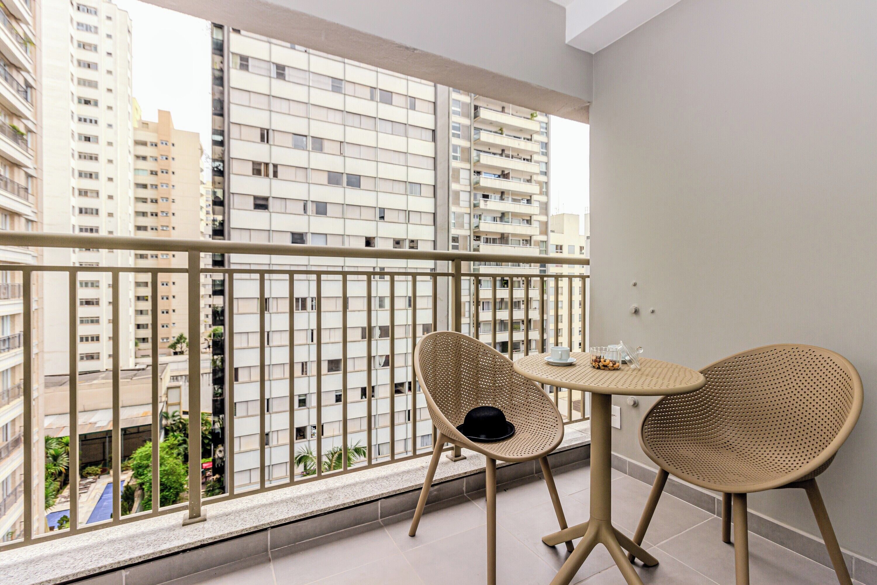 Een balkon met twee rieten stoelen en een kleine tafel, met uitzicht op een stadsgezicht met hoge gebouwen.