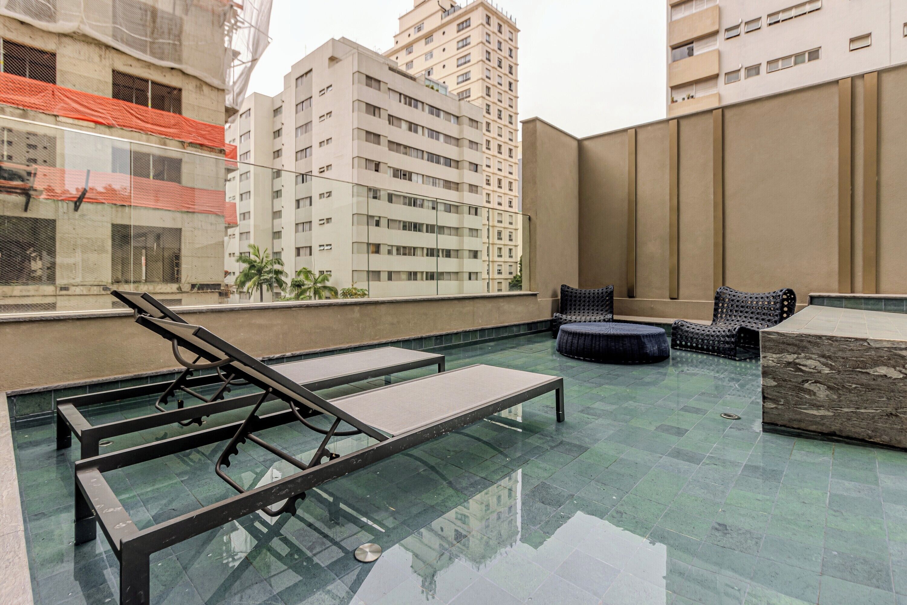 A rooftop pool area with lounge chairs and a glass table.