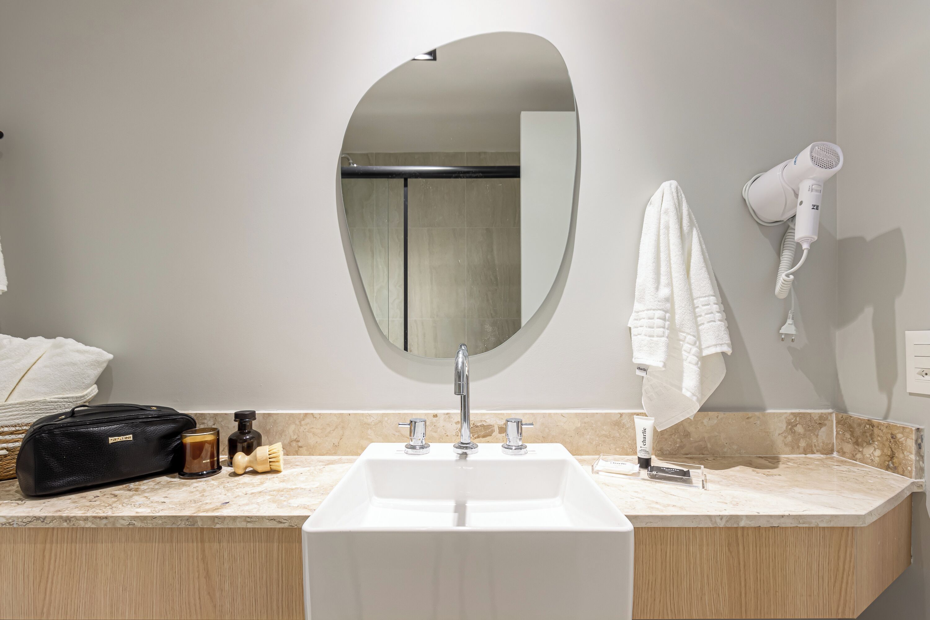 A bathroom with a white sink, a mirror, a towel rack, a hairdryer, and toiletries on the counter.