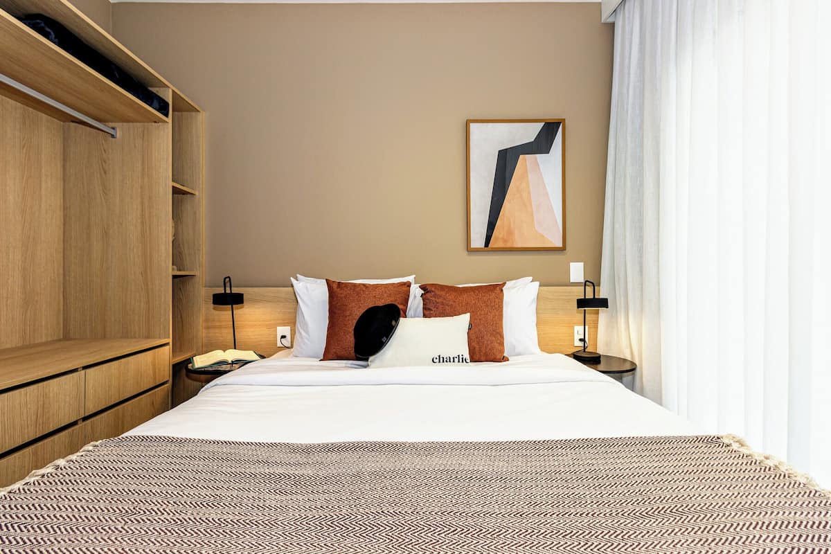 A hotel room with a bed, a nightstand, a lamp, a wooden wardrobe, and a painting on the wall.