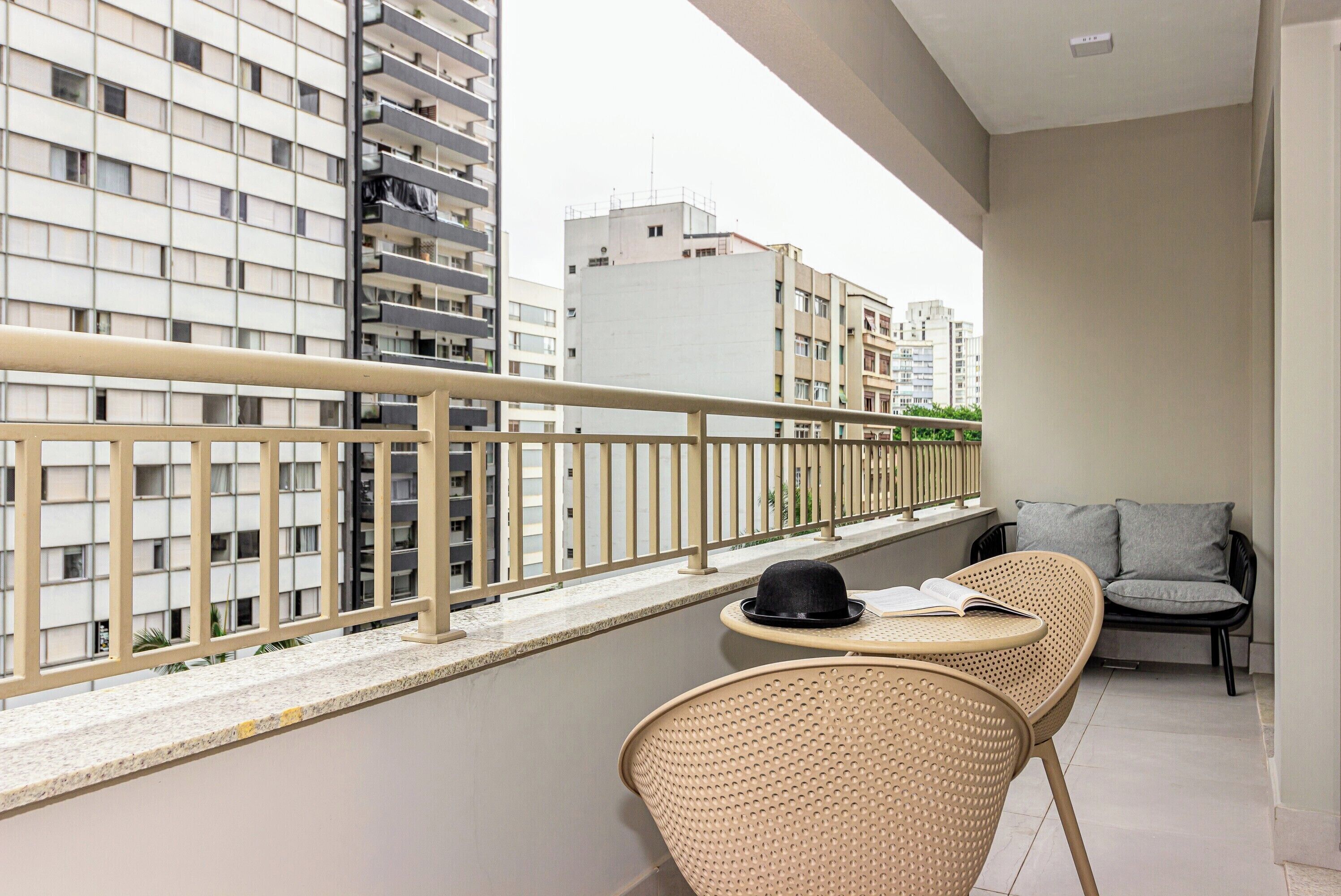 A balcony with a railing, two wicker chairs, a small table, and a book.