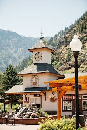 A building with a clock tower, a wooden pergola, and a stone waterfall feature.