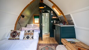 Une chambre à coucher confortable et compacte, comprenant un lit, des oreillers, un bureau et un espace douche.