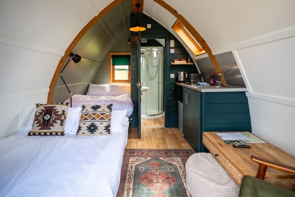 Une chambre à coucher confortable et compacte, comprenant un lit, des oreillers, un bureau et un espace douche.