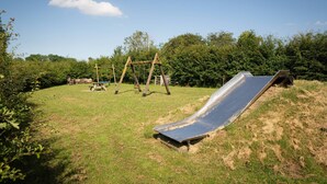 Une aire de jeux avec un toboggan, des balançoires et une table de pique-nique, le tout installé dans un espace verdoyant.