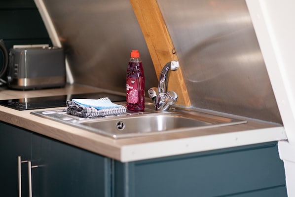 A kitchen with a stainless steel sink, a toaster, and a bottle of red drink. - Luxury Cosy Cabin with Hot Tub in Rural Yorkshire (Northallerton)