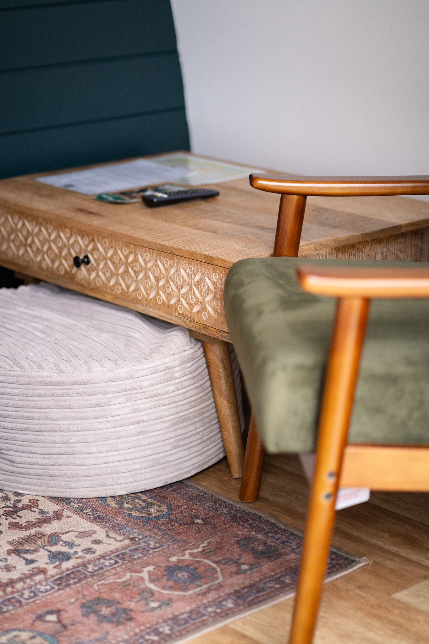 A bed with a wooden headboard, a green upholstered chair, a wooden side table, and a patterned rug on the floor.