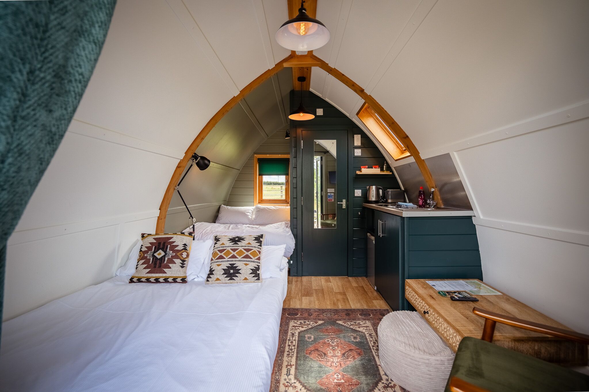 Un dormitorio acogedor en el ático, con techo inclinado, una cama con almohadas estampadas, un escritorio pequeño y vistas a la cocina.