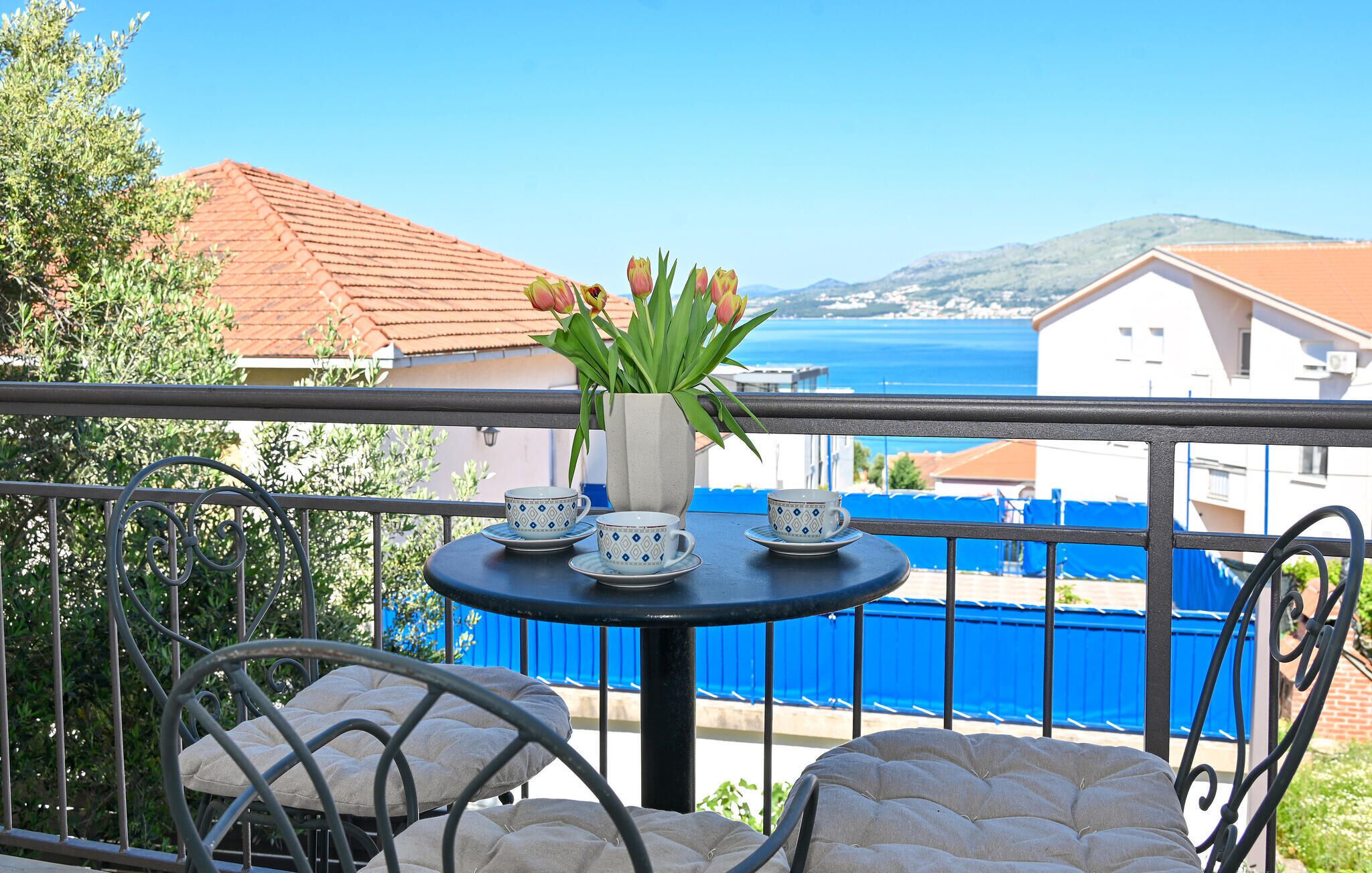 Un balcon avec une table dressée pour deux personnes, un vase de tulipes et une vue sur la mer et les bâtiments.
