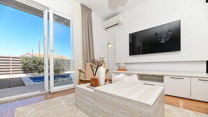 Un salon moderne doté d’un grand téléviseur, d’une porte vitrée donnant sur un balcon et d’un design minimaliste.