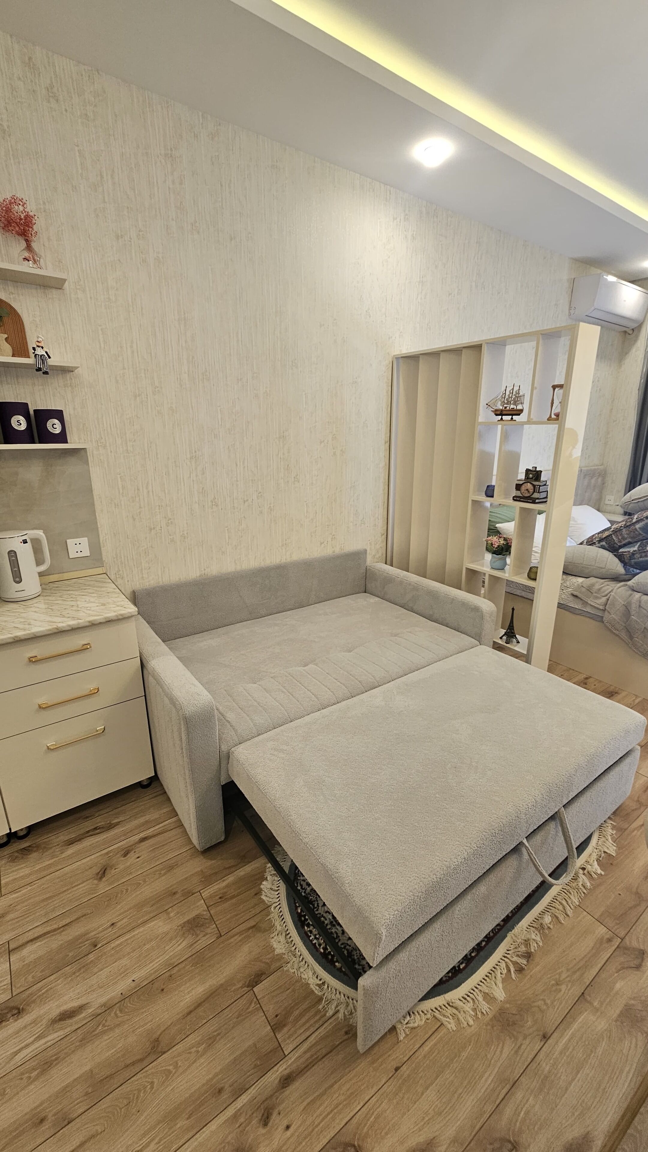 A modern bedroom with a bed, bedside table, and a small shelf with decorative items.