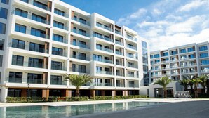 Ein modernes, mehrstöckiges Hotel mit Poolbereich, mit Balkonen und blauem Himmel.