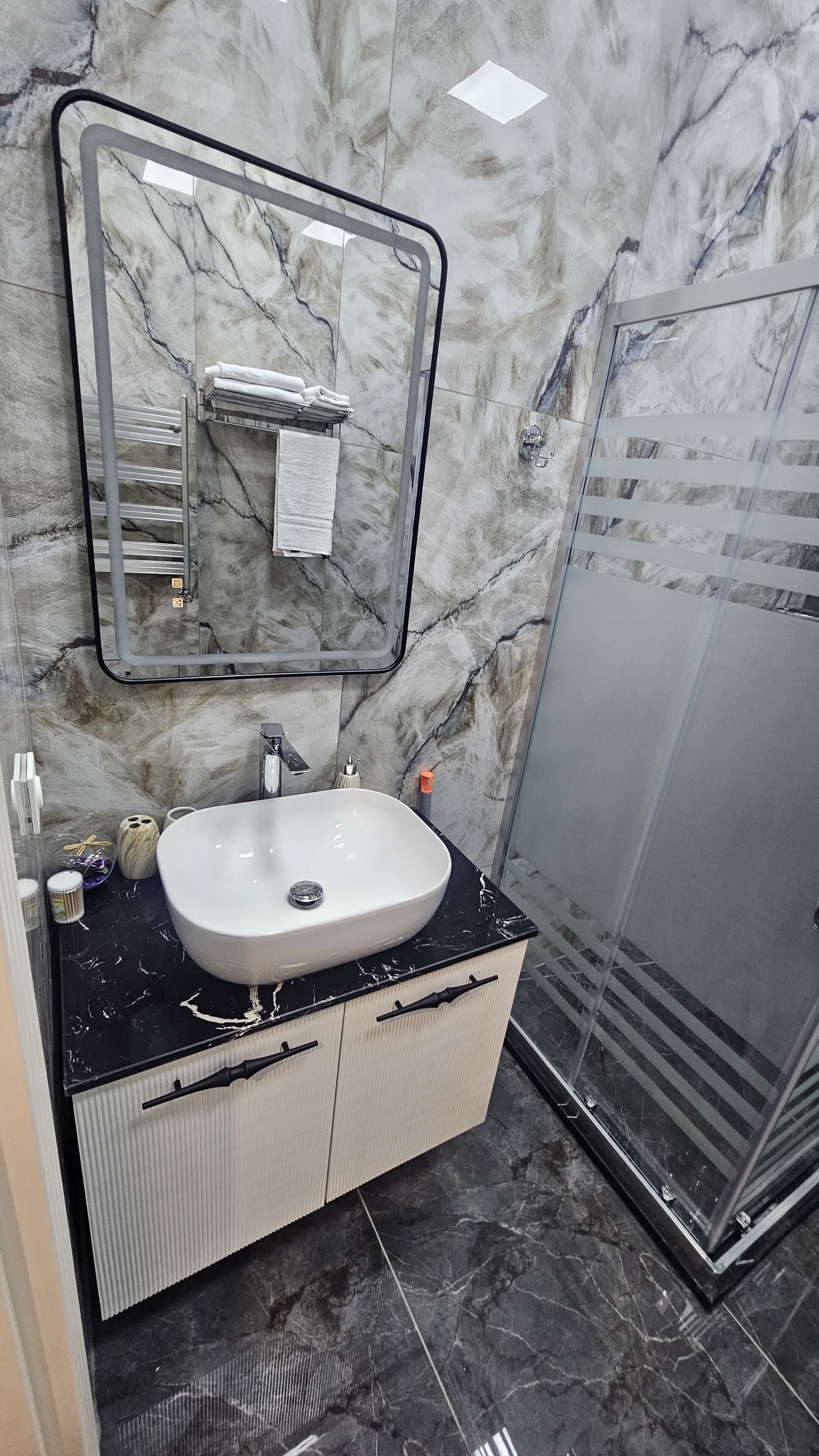 A bathroom with a marble wall, a white sink, a glass shower enclosure, and a towel rack.
