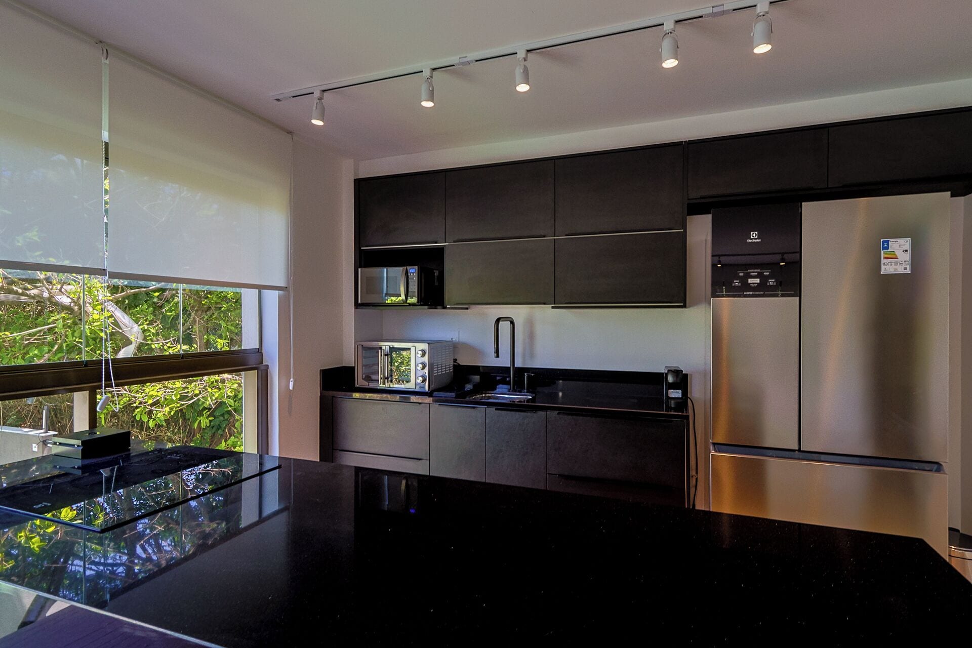 A modern kitchen with a black countertop, stainless steel appliances, and a window overlooking greenery.