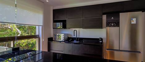 A modern kitchen with a black countertop, stainless steel appliances, and a window overlooking greenery.