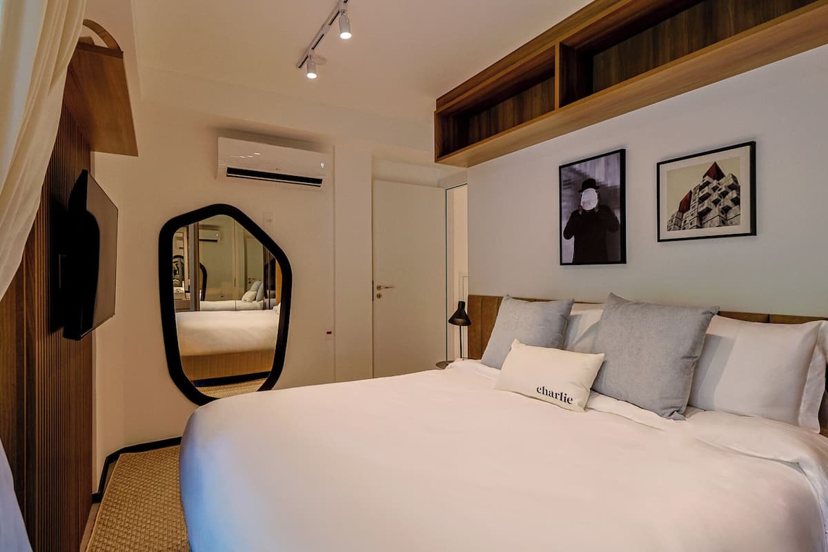 A bedroom with a large bed, a mirror, an air conditioning unit, and two framed pictures on the wall.