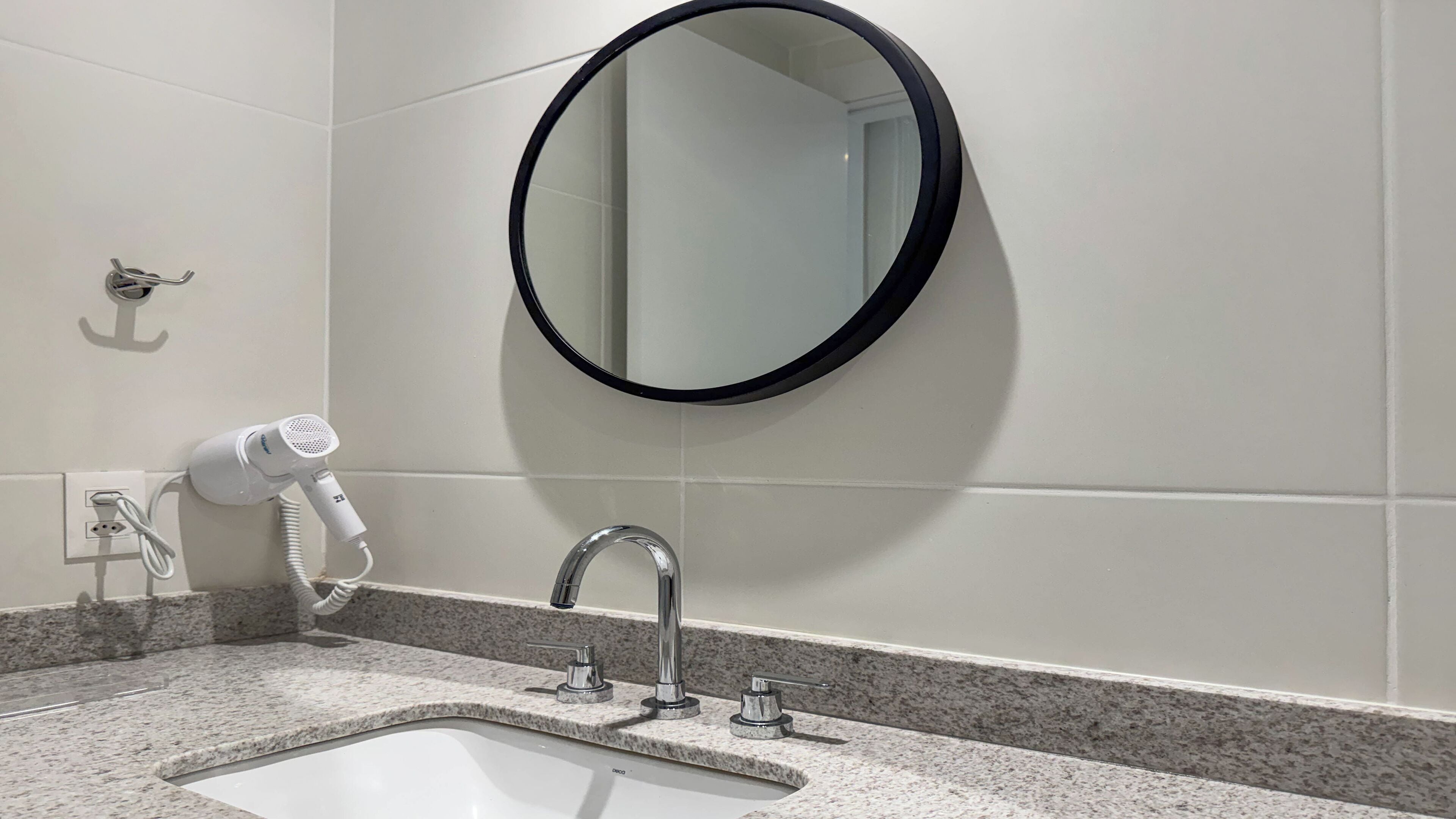 A bathroom with a white sink, a round mirror, and a hairdryer plugged into a wall socket.