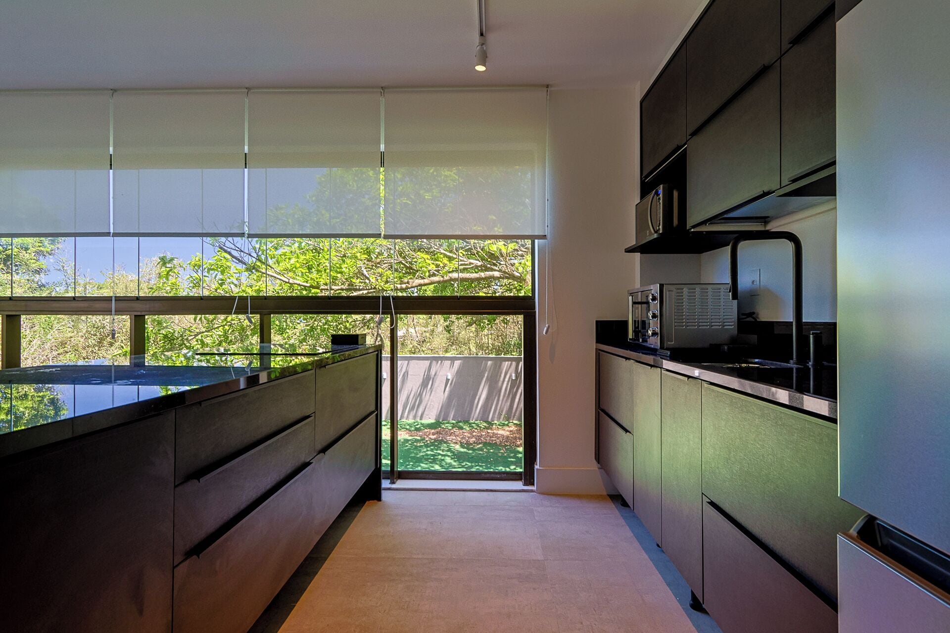 Eine moderne Küche mit großem Fenster, dunklen Schränken und Blick auf Grünfläche.