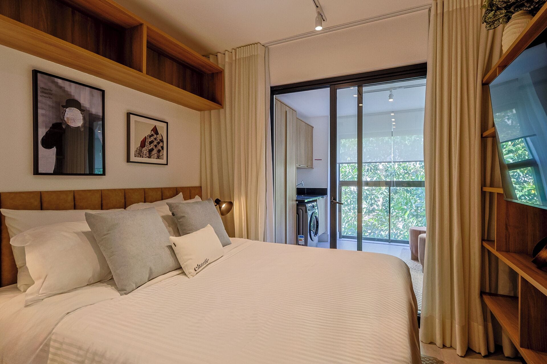 Une chambre avec un grand lit, une tête de lit en bois, un lave-linge et une vue sur la verdure.